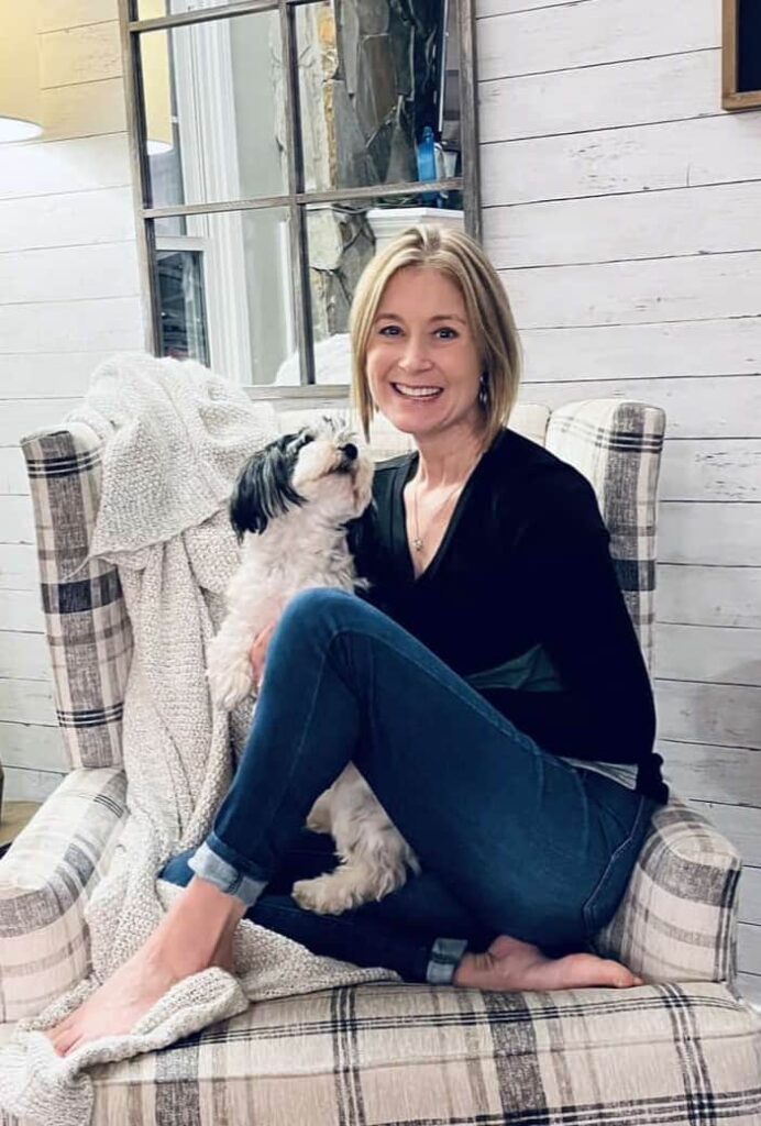 caucasian woman wearing black v-neck long-sleeved shirt sitting crossed legged with a black and white havanese dog in her lap
