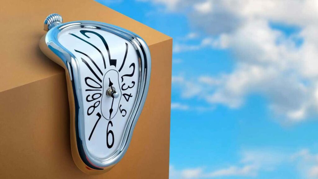 Melted clock on a cardboard box against a blue sky with white clouds in the background.