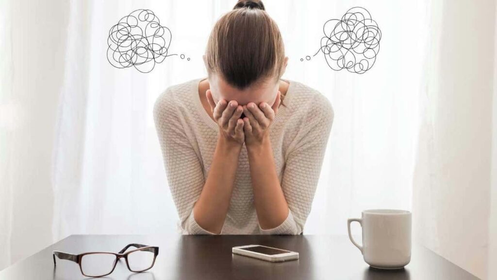 Woman wearing hair in a bun with her elbows on the table and head in her hands.