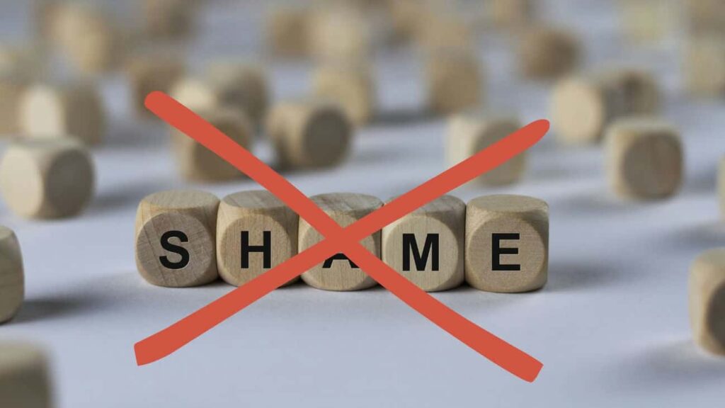 Wooden cube letters spelling the word "shame" with a large red X crossing it off.